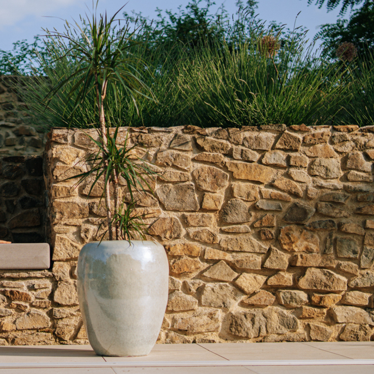 Pot GALILEE décoratif 50x60 cm perle en terre cuite émaillée, près d’un mur en pierre