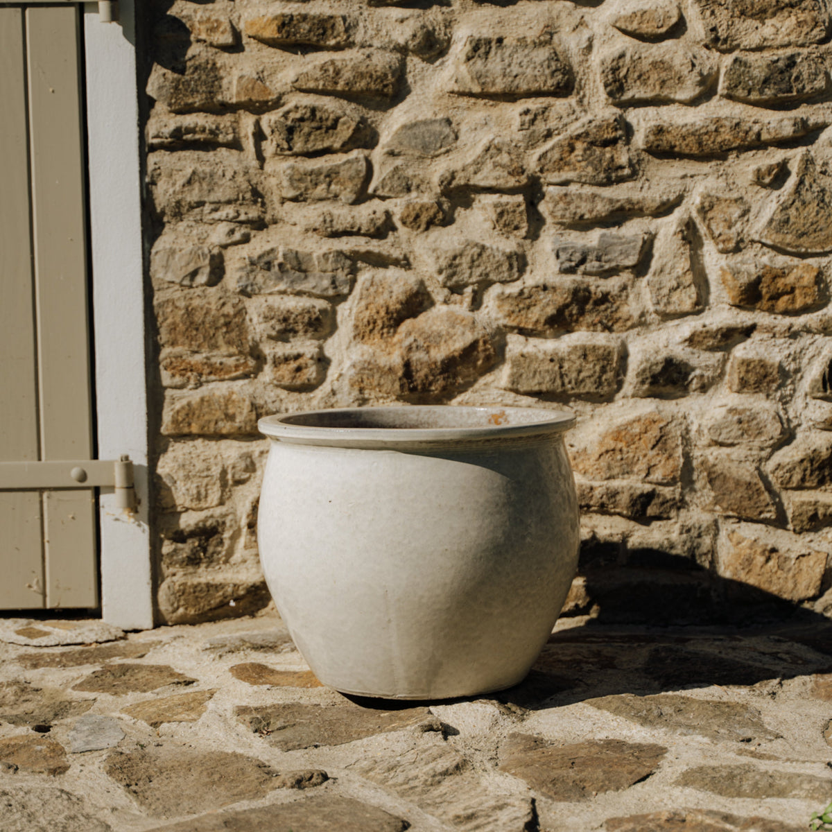 Pot NEWTON rond 44x35 cm crème en terre cuite émaillée, vue de face contre un mur en pierre