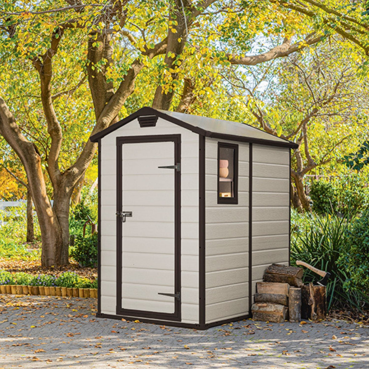 Abri de jardin MANOR 4x6 beige installé sous des arbres dans un jardin