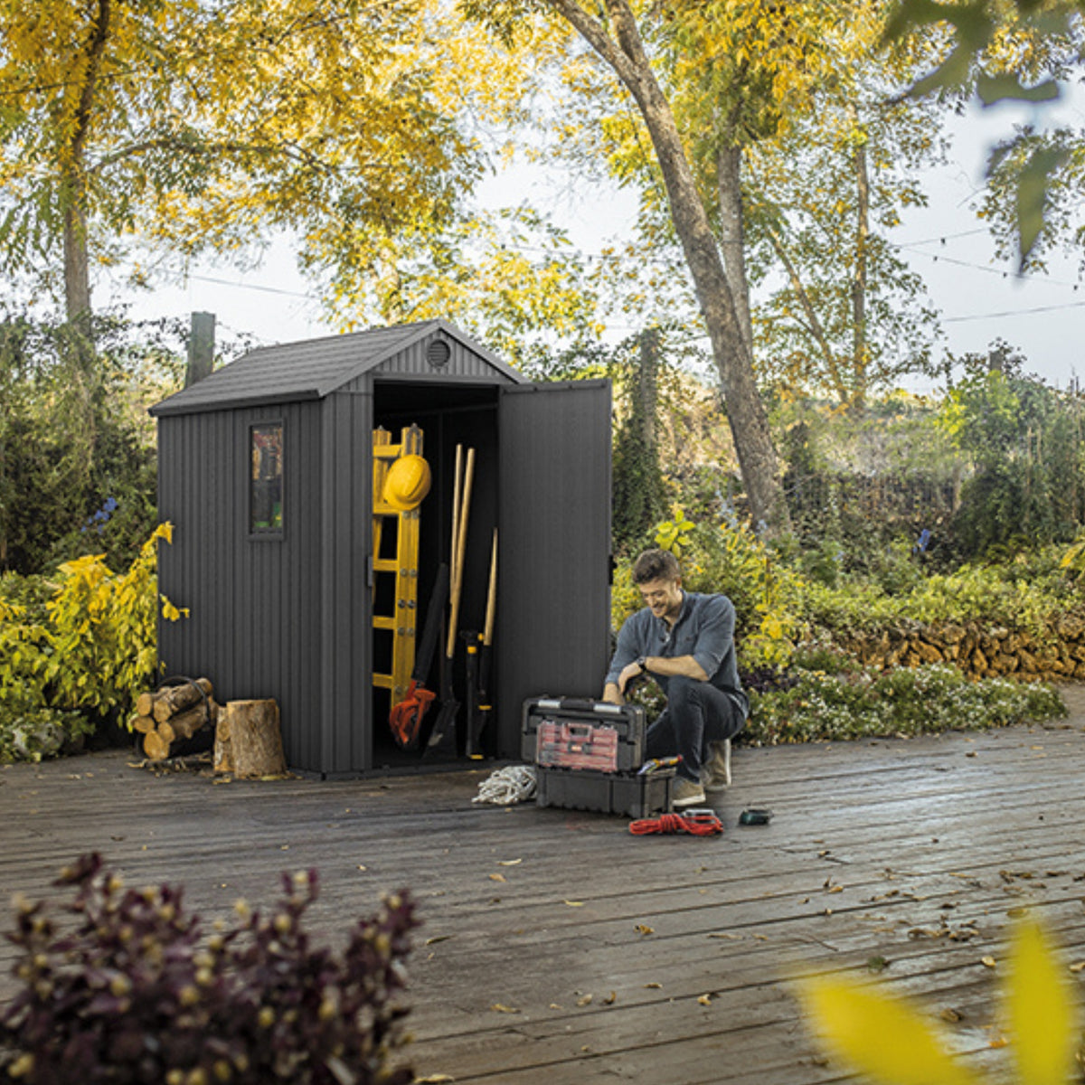 Abri Darwin sombre ouvert sur une terrasse avec outils de jardin et un homme assis