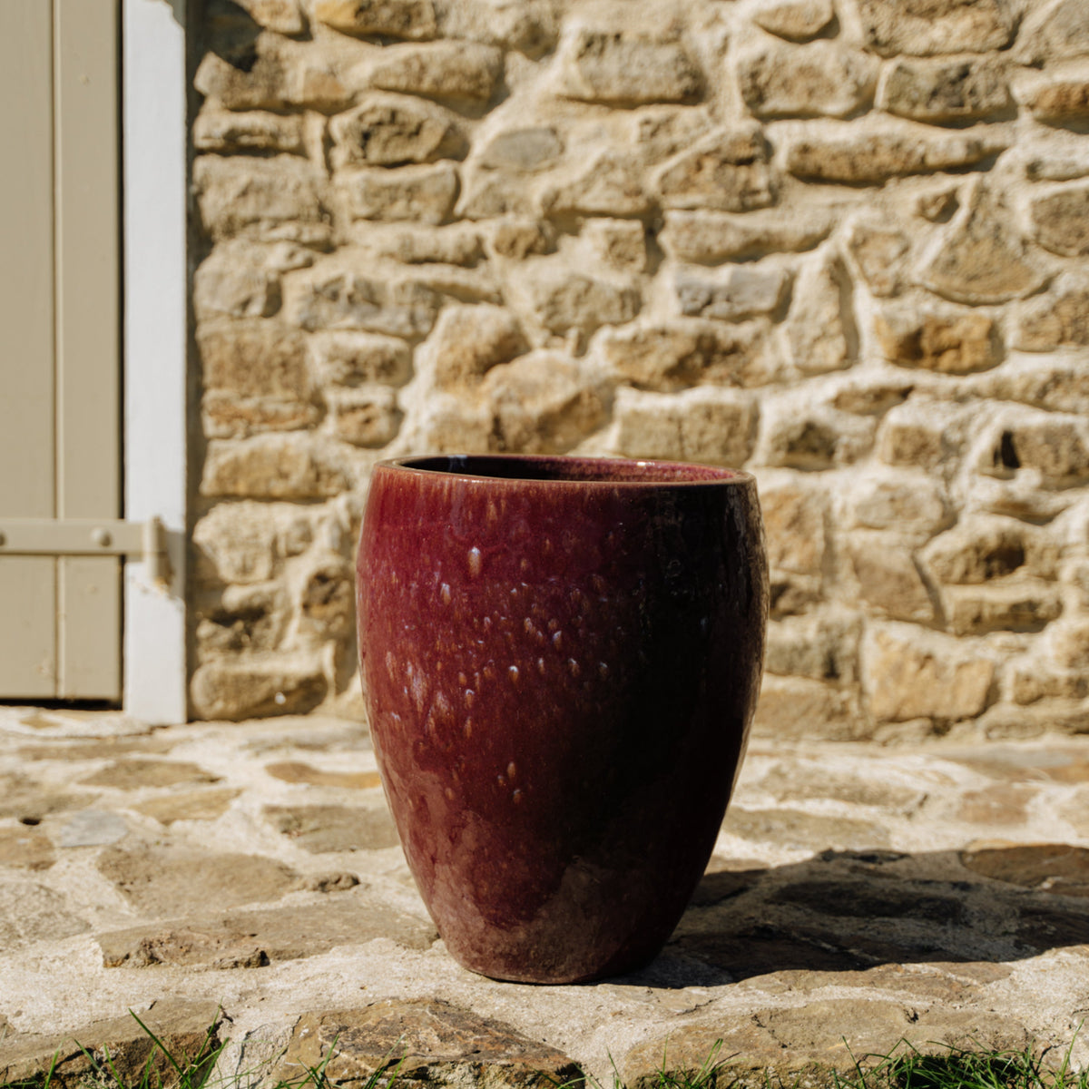 Macetero LAFONTAINE con forma de ánfora 23 × 35 cm violeta claro de cerámica esmaltada, vista frontal en un patio