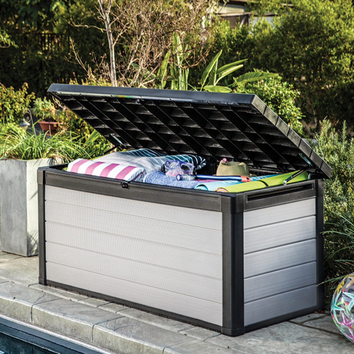 Coffre Denali DuoTech gris ouvert rempli de coussins au bord d'une piscine