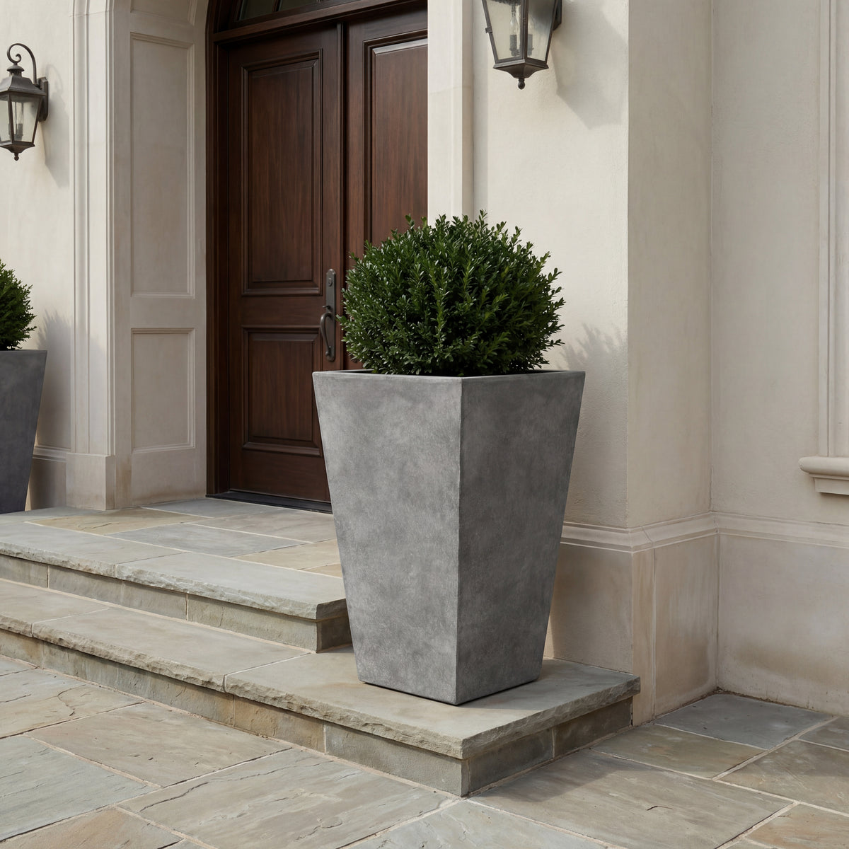Pre-drilled rectangular Aeris cachepot light grey in fibre concrete, with shrub in front of an entrance