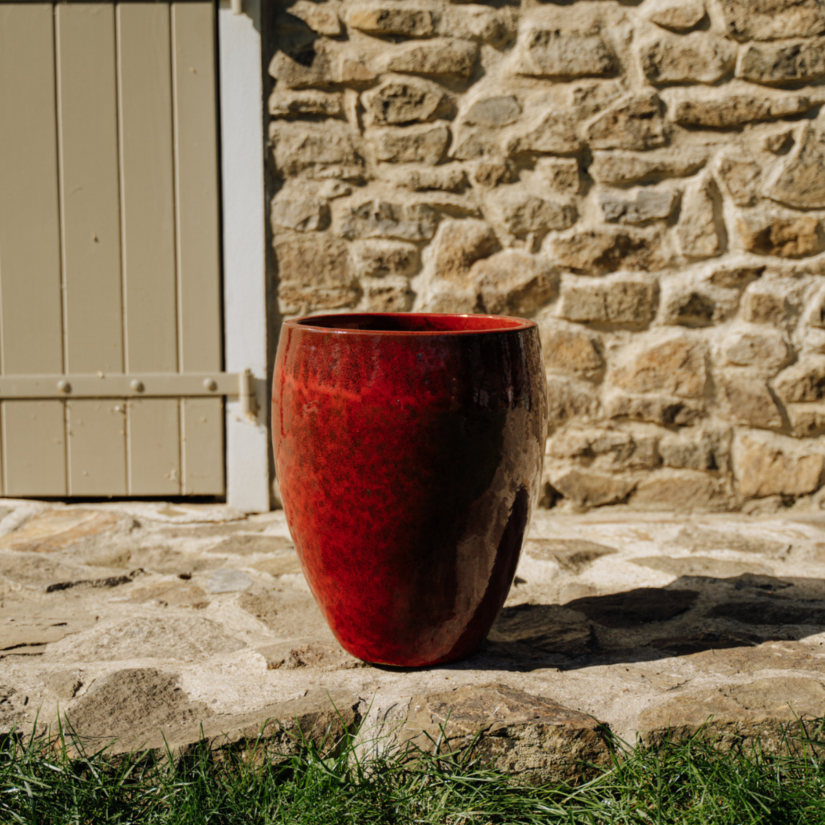 Ronde plantenbak Poseidon2 36 × 43 cm Tropisch rood van geglazuurd keramiek, geplaatst voor een stenen muur
