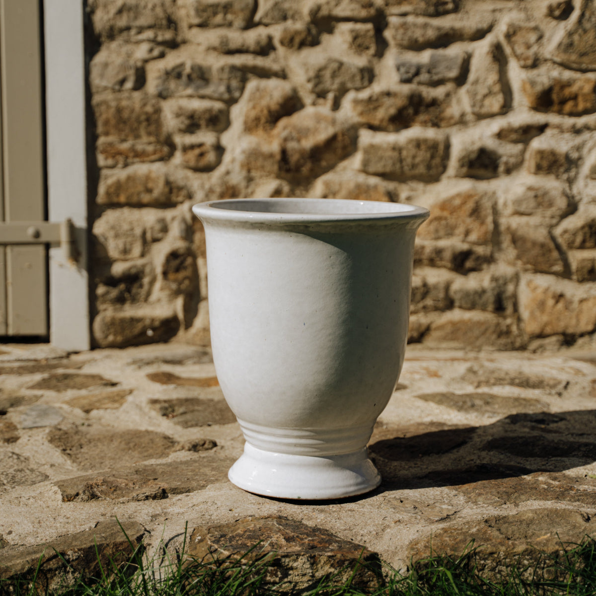 Pot Arthur avec pied 32x39 cm blanc en terre cuite émaillée, posé sur une terrasse en pierre