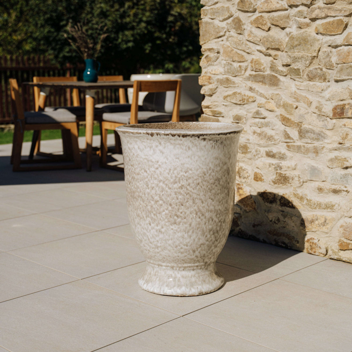 Plantenbak Arthur met voet 42x52 cm gestreept wit van geglazuurd keramiek, geplaatst op een terras bij een muur