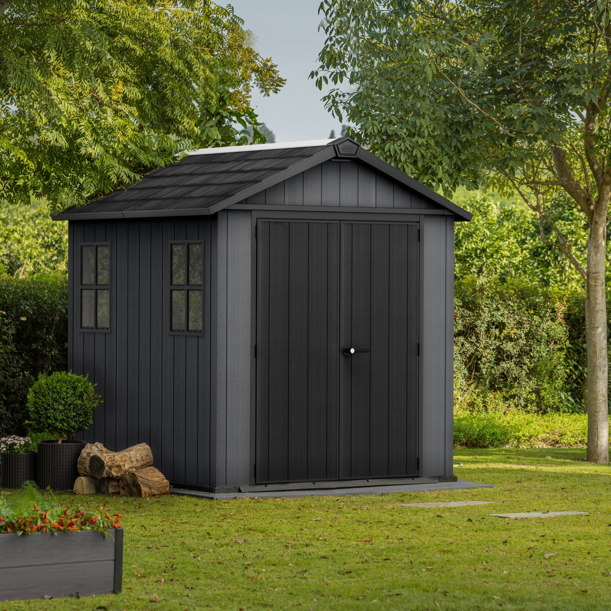 Abri de jardin gris installé sur une pelouse, vu de face avec fenêtres