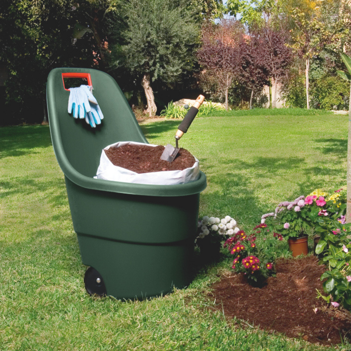Carretilla Easy Go verde llena de sustrato en un jardín florido