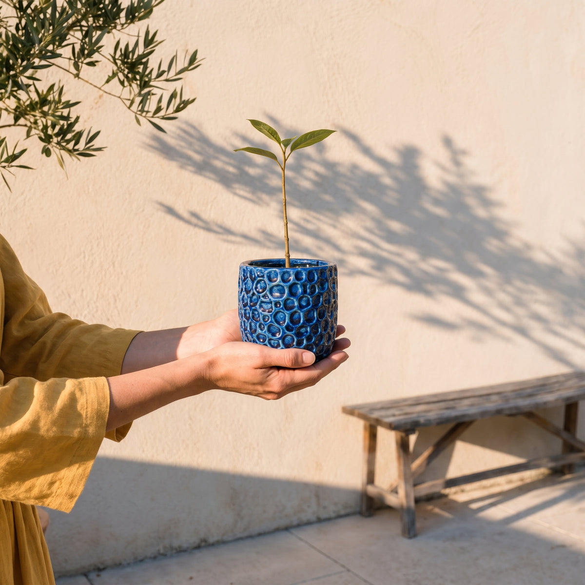 Pot PARISETTE rond 12x10 cm bleu en terre cuite émaillée, tenu en mains sur terrasse