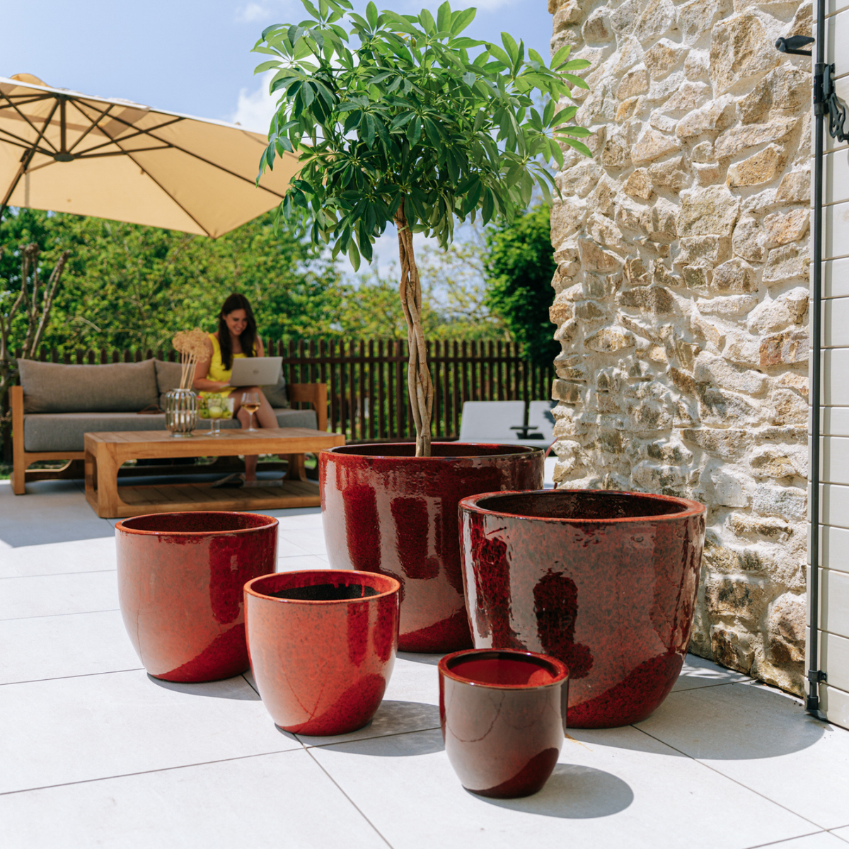 Macetero LANCELOT decorativo 36 × 34 cm rojo tropical de cerámica esmaltada, entre varios maceteros en una terraza