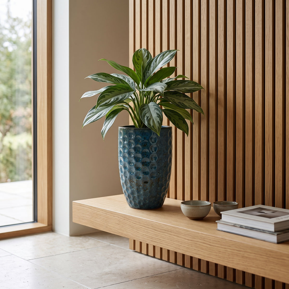 Amfoorvormige plantenbak Merovee 23x35 cm Staalblauw van geglazuurd keramiek, met groene plant op een sidetable binnenshuis
