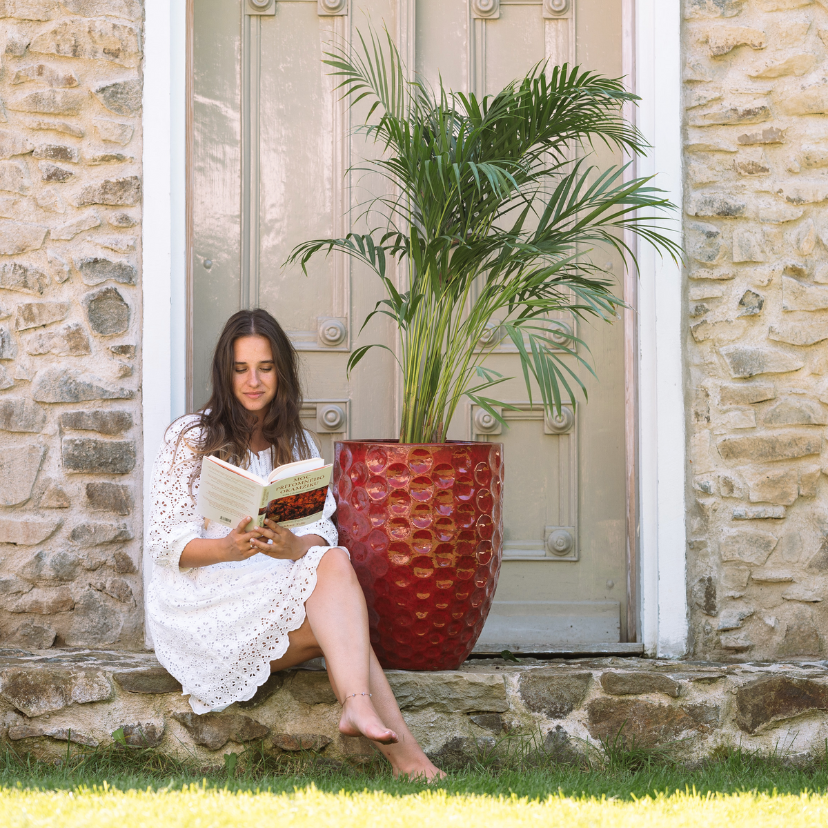 Macetero Merovee con forma de ánfora 42x55 cm rojo tropical de cerámica esmaltada, con palmera frente a una puerta