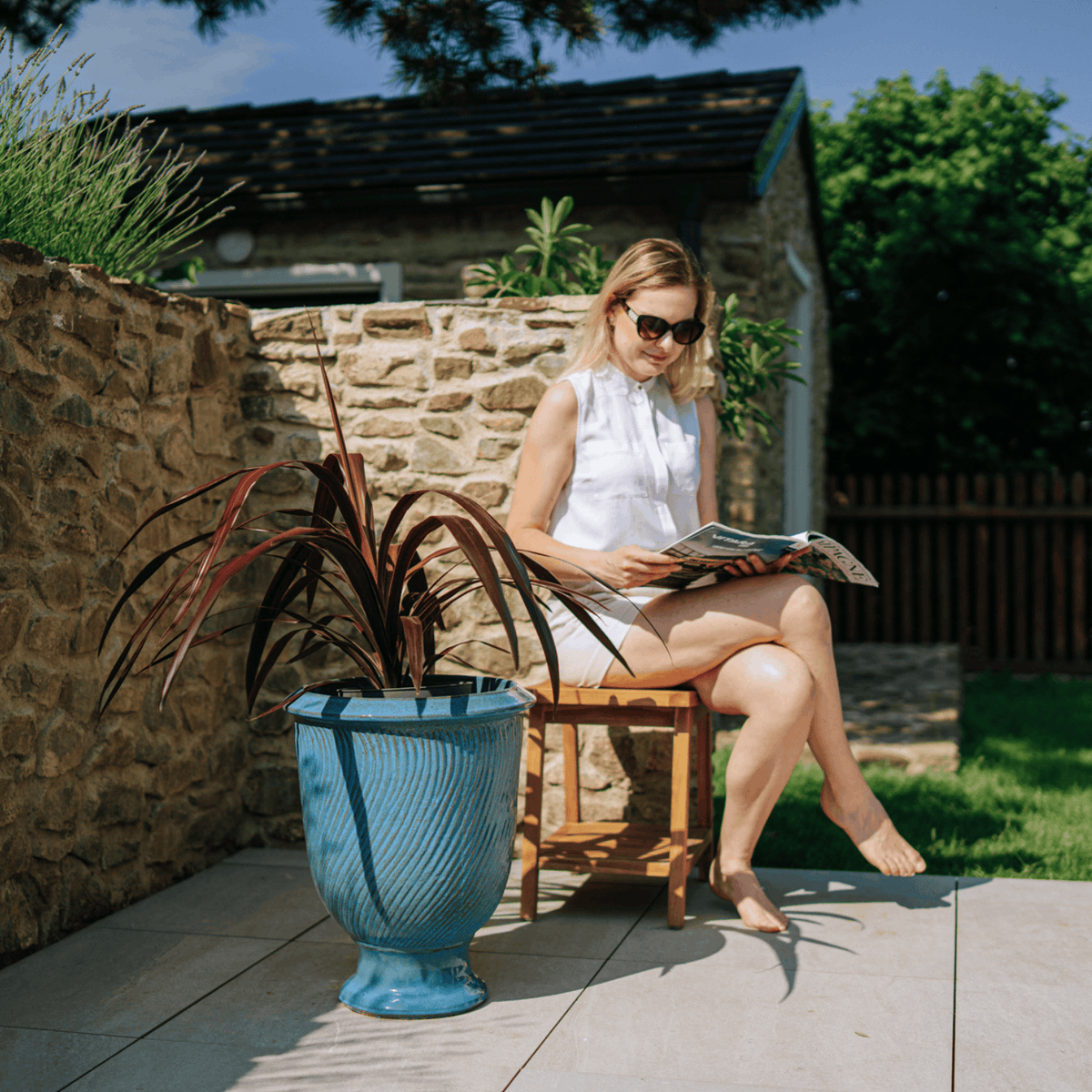 Pot Morgane avec pied 42x52 cm bleu acier en terre cuite émaillée, plante aux feuilles bordeaux sur terrasse