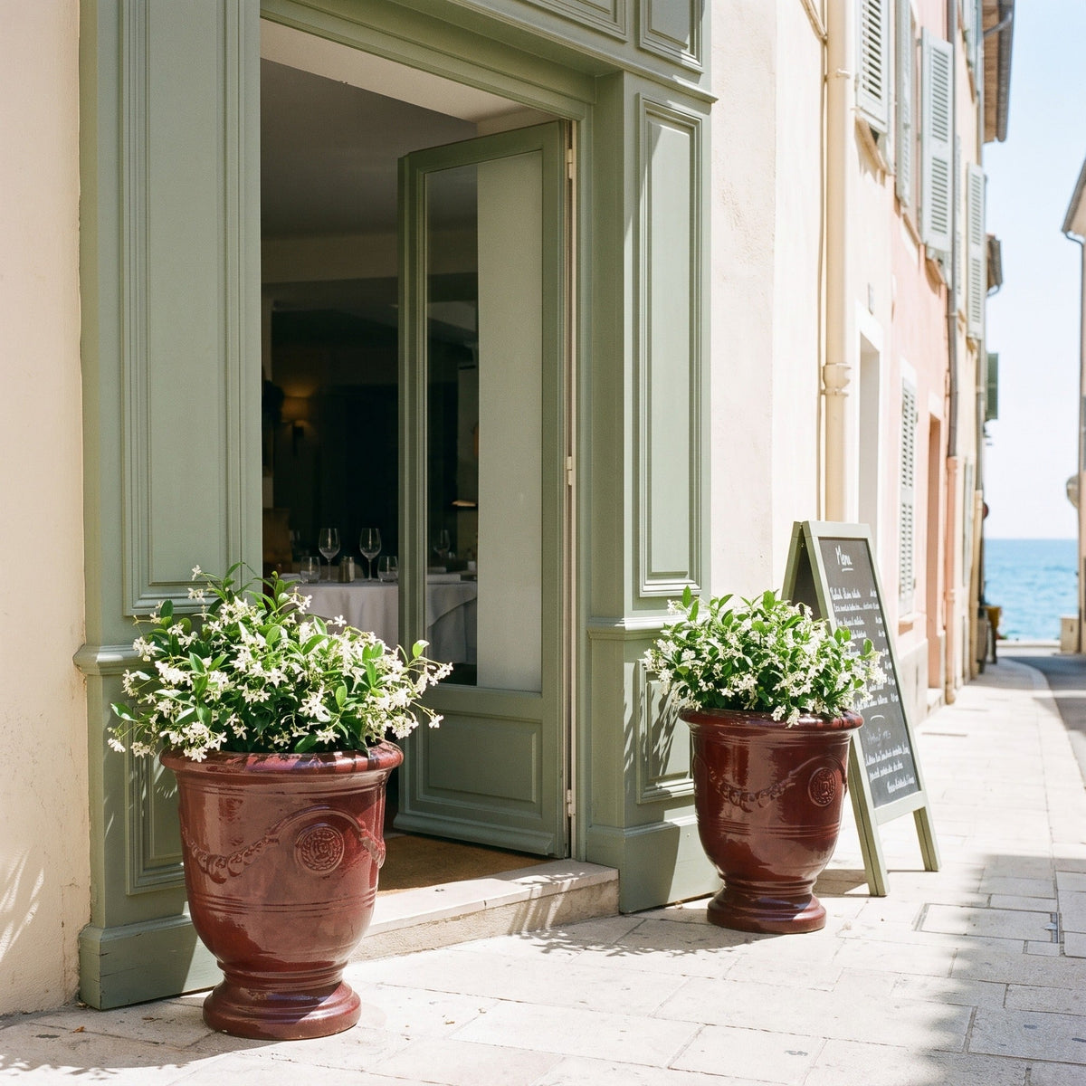 Vaso Richelieu con piede 46x56 cm Rosso mattone in ceramica smaltata, fiori bianchi davanti all'ingresso di un ristorante