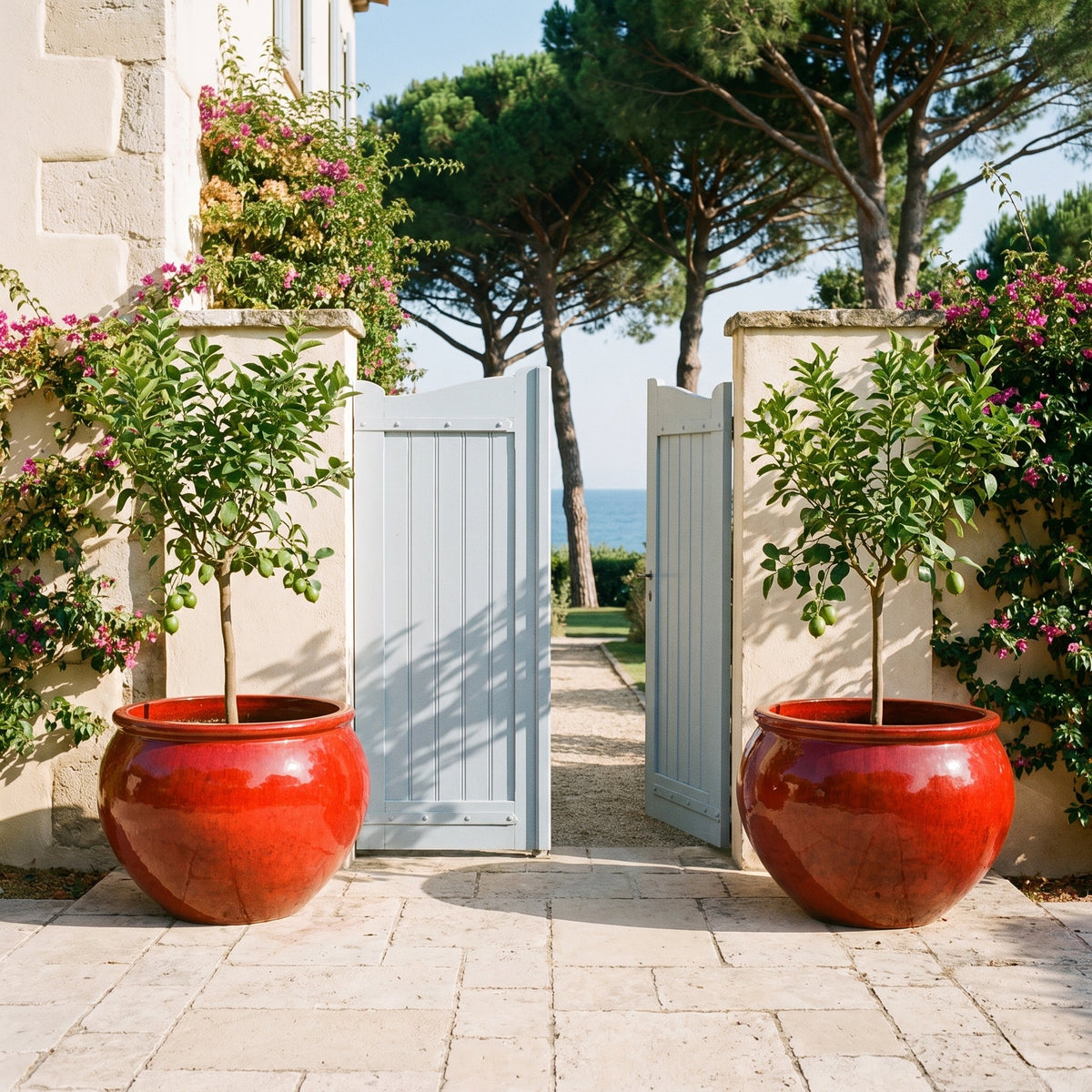 Round LUTECE planter 86x64 cm in Tropical Red glazed ceramic, with small trees in front of a gate