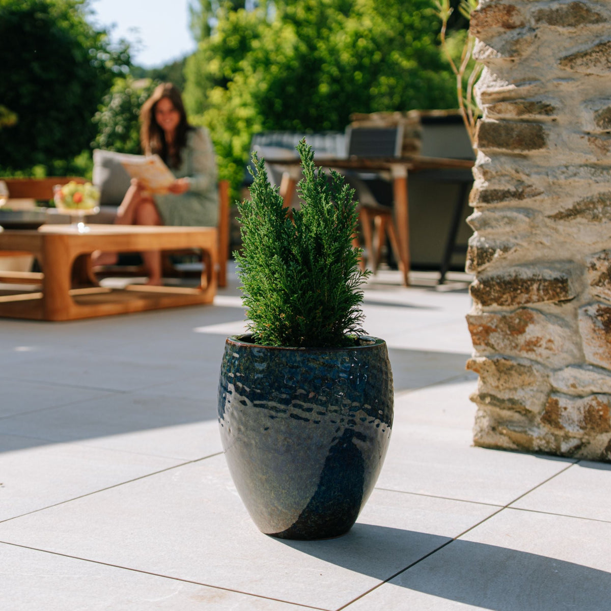 Macetero POSEIDON2 redondo 28 × 31 cm azul abismo de cerámica esmaltada, en una terraza con conífera