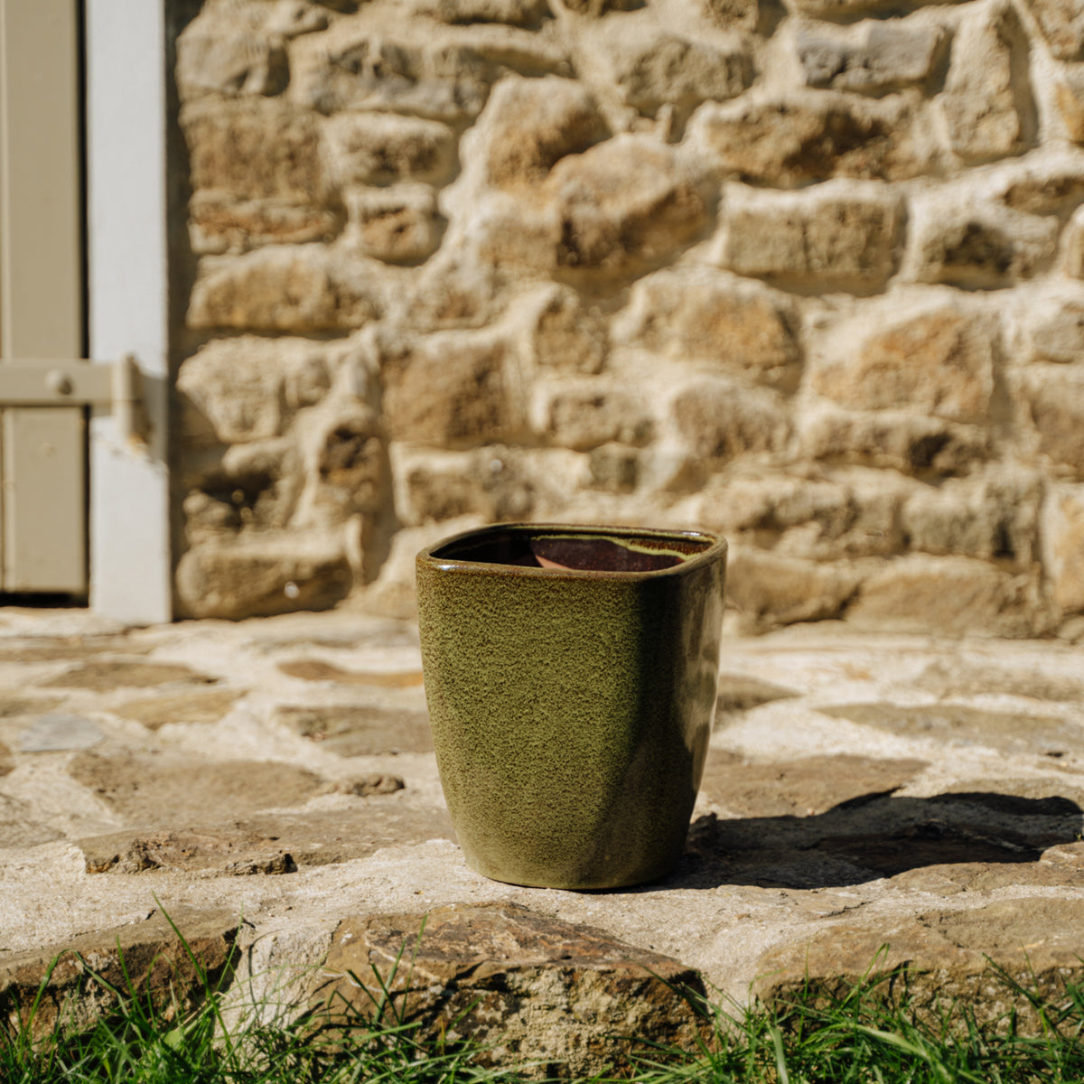 Pot Vauban rectangle 18x21 cm vert de lac en terre cuite émaillée, posé devant un mur en pierre